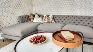 A modern living room with a grey sectional sofa, a round coffee table with a white marble top, and a small side table with a book and a candle. - Tranquil 4-Bed Oasis Modern & Chic (Oxford)