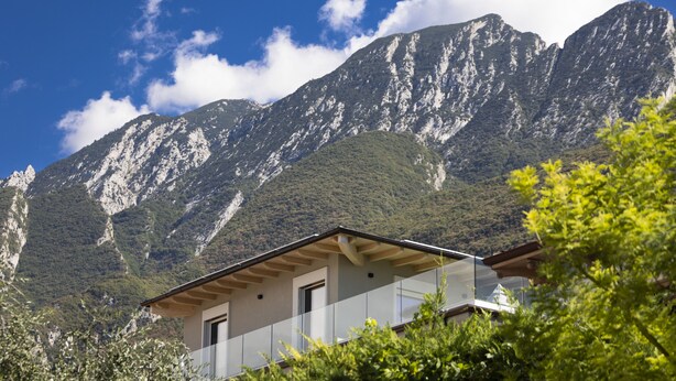 A mountain cabin with a balcony, surrounded by lush greenery and a clear blue sky.