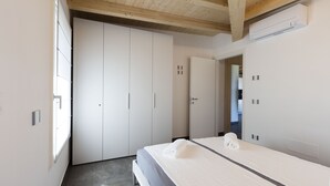 A modern bedroom with a large wardrobe, a bed with a neatly folded towel, and an air conditioning unit on the wall.