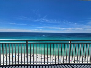 A beach view from a balcony with a railing, clear sky, and ocean.