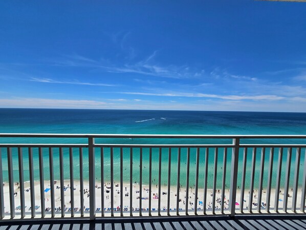 Blick auf einen Strand vom Balkon mit Geländer, klarer Himmel und Meer.