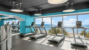 A gym with treadmills and exercise equipment, large windows with a beach view, and a modern ceiling design. - Splash Resort 1403E 🏖 Beachfront Luxury & Free Chairs ✨️ Mega Vacations PCB (Panama City Beach)