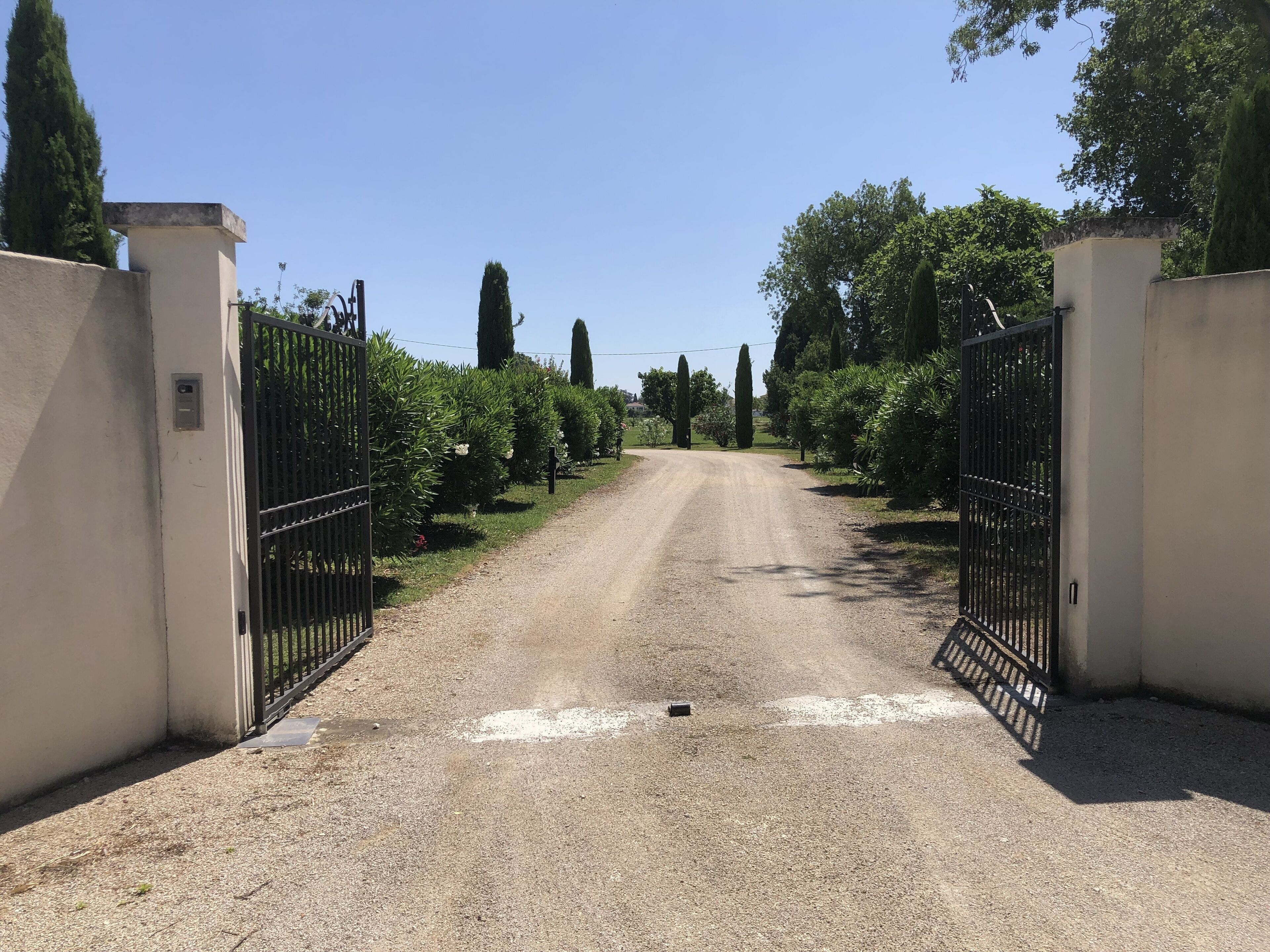 A gravel driveway leading to a gated entrance with a white wall on one side and a metal gate on the other.