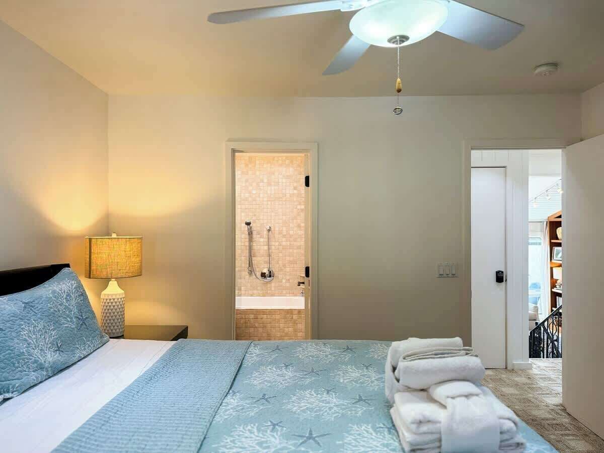 A bedroom with a bed, a nightstand with a lamp, a shower area, and a door leading to another room.