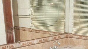 Un baño con lavamanos curvo, un espejo y una ventana con persianas.