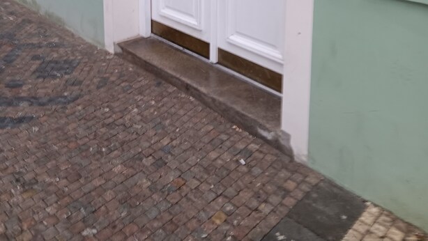 Une entrée d’immeuble avec une façade verte, des portes blanches et un portail en métal.