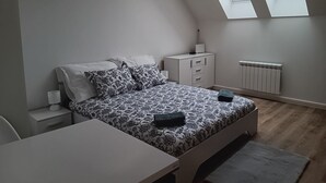Une chambre à coucher comprenant un lit, un bureau, une table de chevet, un radiateur et deux fenêtres de toit.