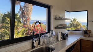 A kitchen with a large window offering a view of palm trees and mountains. - 3-bedroom  w/ amazing views, waterfront access, resort amenities & hot/cold tub (El Sargento, La Ventana)