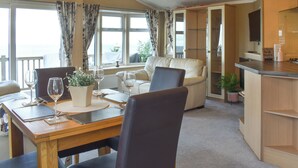 Een eetgedeelte met een tafel gedekt voor twee personen, een bank en een keuken met een aanrecht en kastjes.