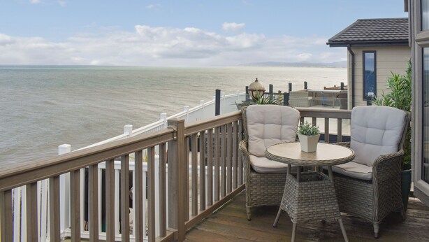 A balcony with wicker chairs and a small table, overlooking a body of water.