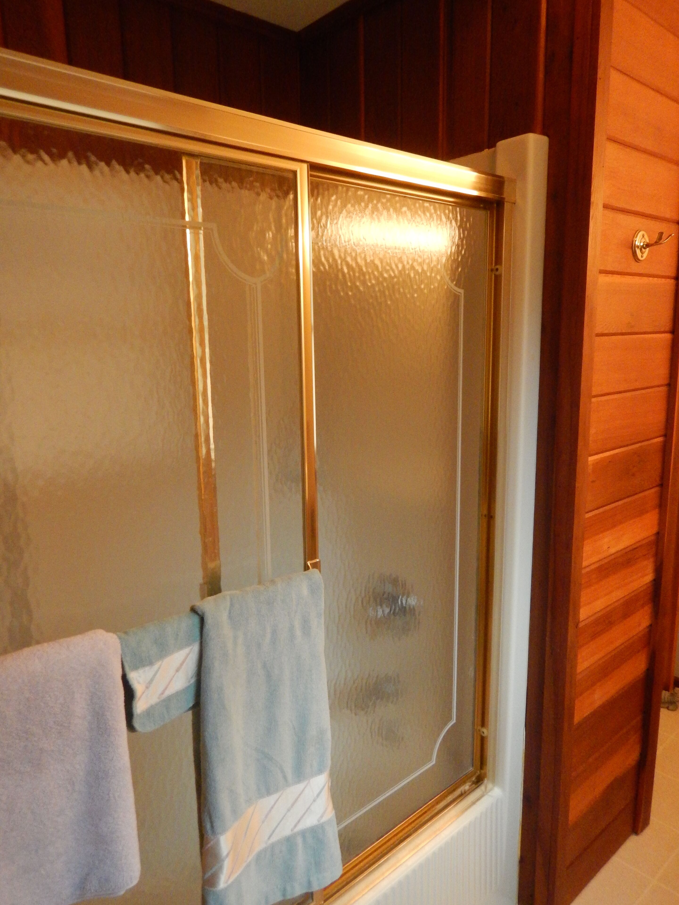 A bathroom with a glass shower enclosure, a towel rack, and wooden paneling on the wall.