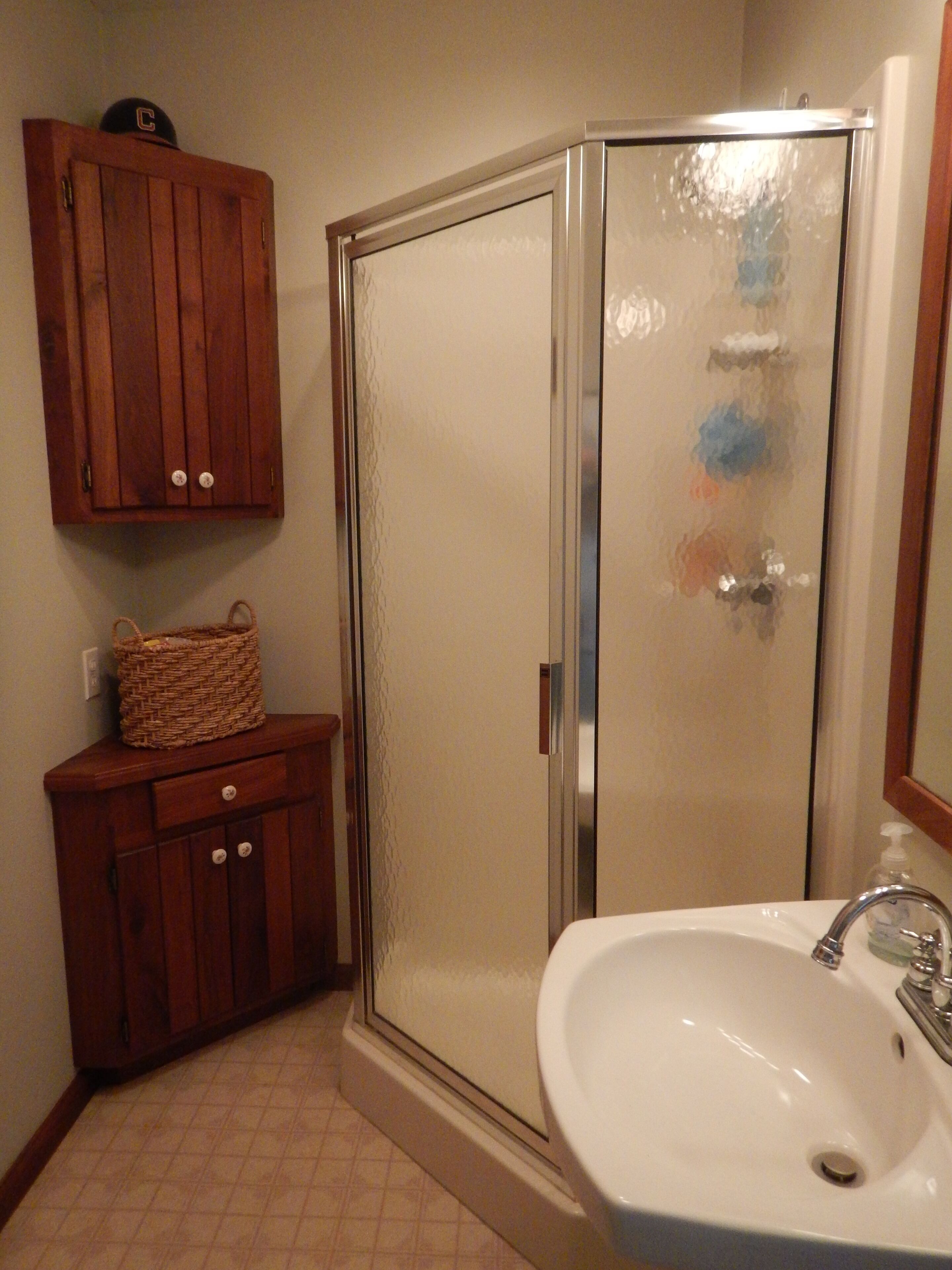 A bathroom with a wooden cabinet, a wicker basket, a glass shower enclosure, and a white sink.