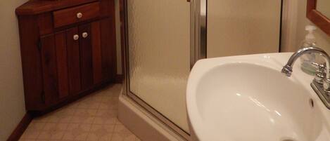 A bathroom with a wooden cabinet, a wicker basket, a glass shower enclosure, and a white sink.