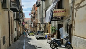 Una estrecha calle empedrada flanqueada por edificios de varios pisos, algunos con balcones y unidades de aire acondicionado.