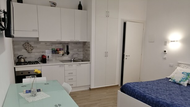 Una habitación compacta con cama, un escritorio pequeño con silla, y una zona de kitchenette.