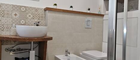 A bathroom with a white sink, two bidets, a mirror, and patterned tiles.