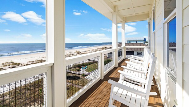 Un balcon avec des chaises blanches, une vue sur la plage et un jardin clos.