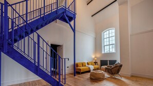 A spacious room with a blue staircase, a yellow sofa, a brown armchair, and a large window. - 5 bedroom accommodation in Seascale (Seascale)