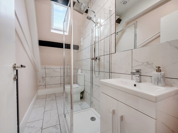 A modern bathroom with a glass-enclosed shower, a white sink, and a marble-tiled floor.