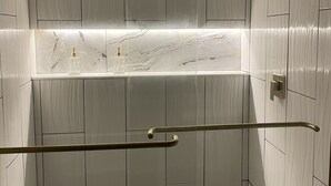 Ett modernt badrum med vita kaklade väggar, en bänkskiva i marmor och en duschhörna med en glasdörr.