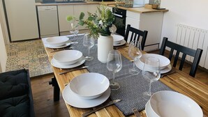 Un coin repas avec une table en bois, dressée pour quatre personnes, entourée de chaises. Un vase blanc contenant des plantes vertes est posé sur la table.