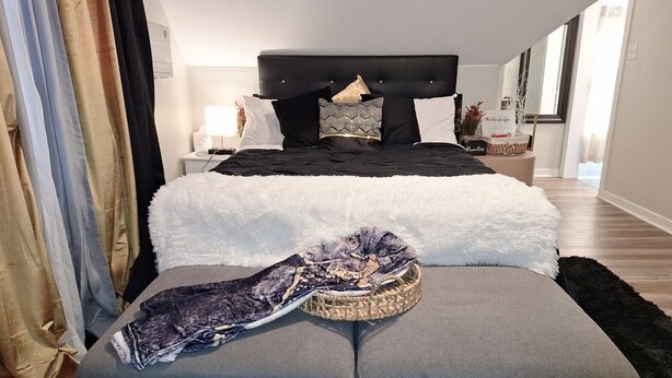 Et moderne soveværelse med en stor seng, en grå sofa og et lille bord med en lampe.