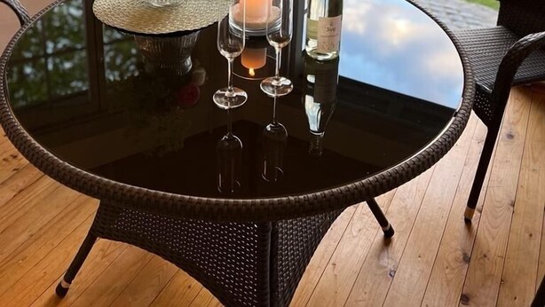 Een ronde glazen tafel met een kaars, een fles wijn en een bloemenvaas.