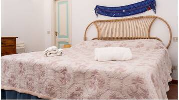 Un dormitorio con una cama, cabecera de madera, lámpara de pared, una puerta y un pequeño aparador de madera.