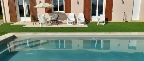 A swimming pool with a patio area, including a table and chairs, and a covered umbrella.