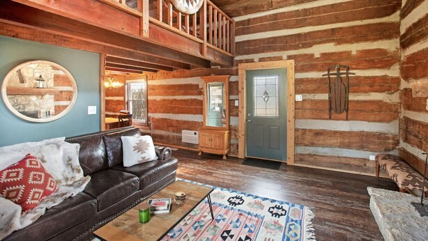 A log cabin interior with a leather sofa, a wooden cabinet, and a patterned rug.