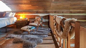 Una habitación de cabaña acogedora con una cama, una silla, una mesita de noche con una lámpara y una colección de peluches.