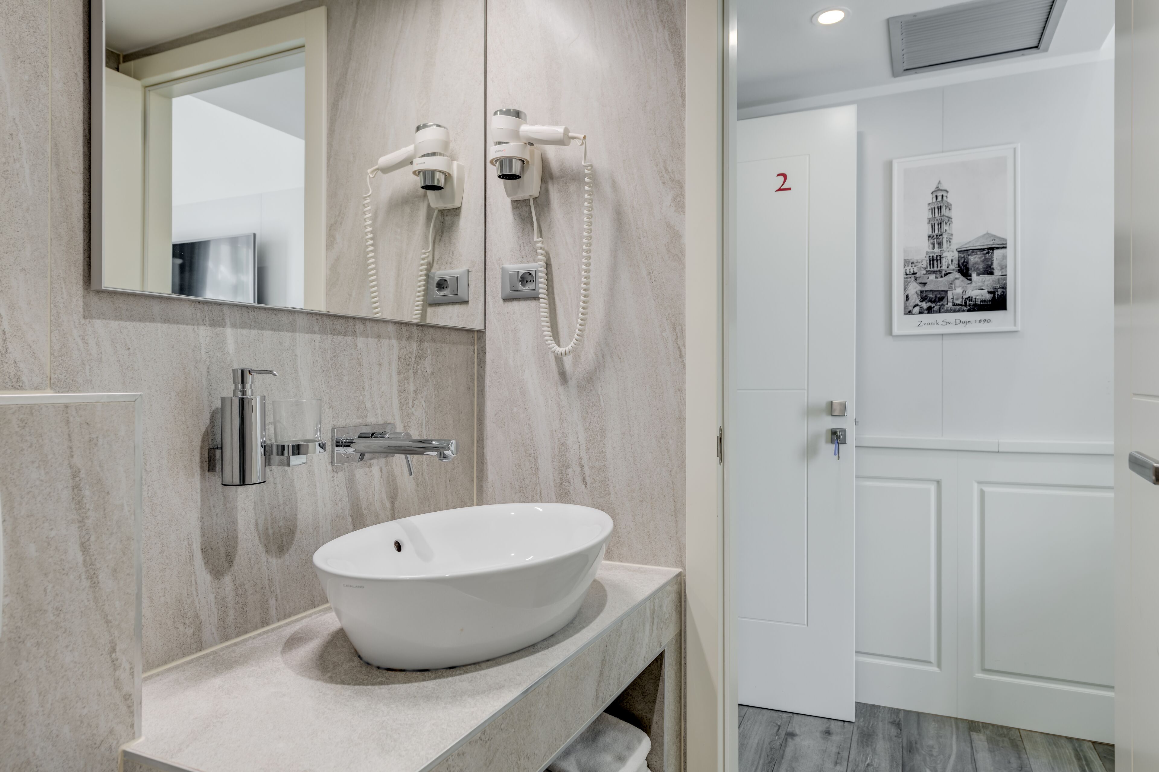 A modern bathroom with a large mirror, a white sink, and a hairdryer mounted on the wall.