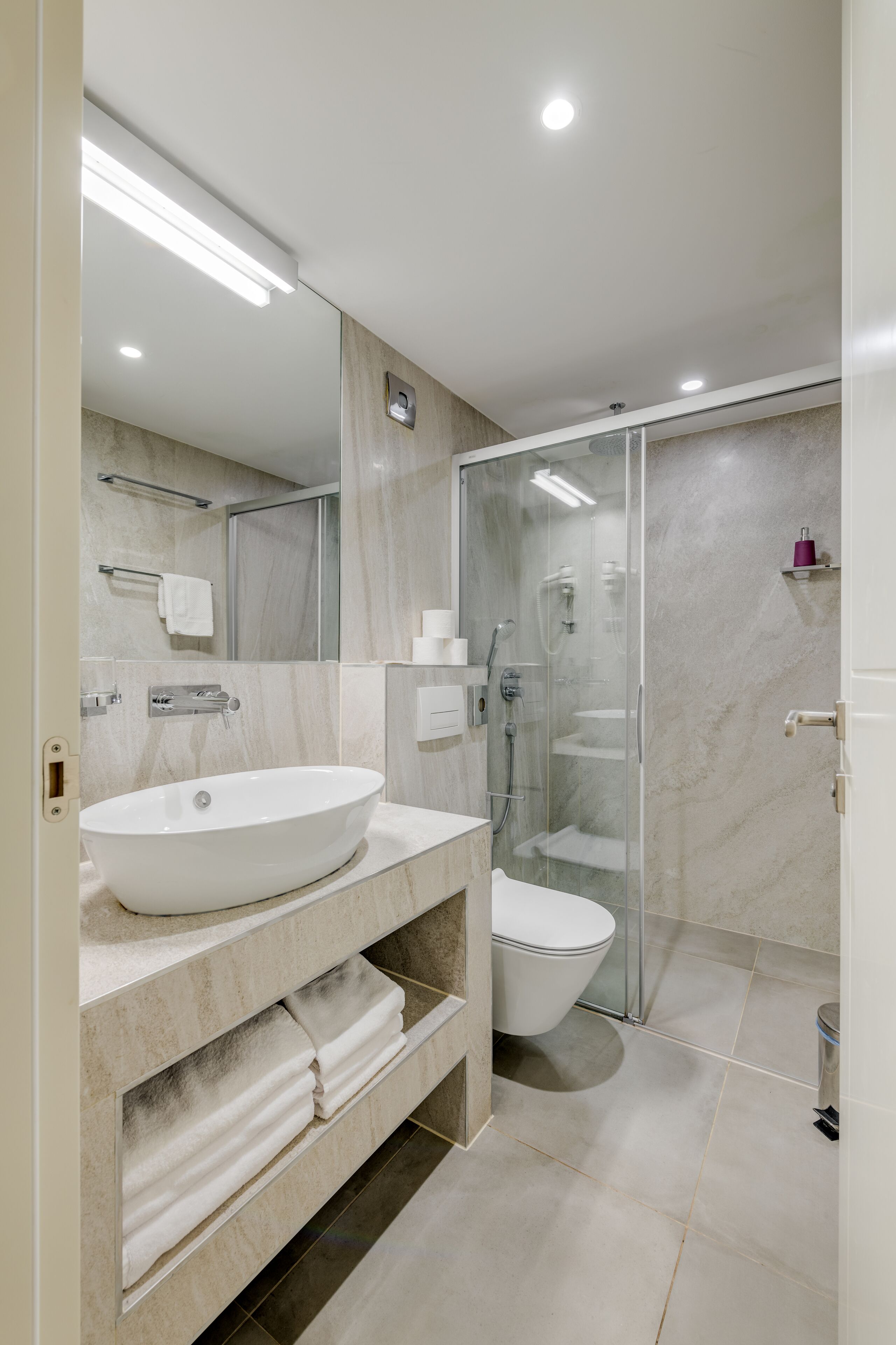Een moderne badkamer met een grote spiegel, een witte wastafel, een toilet en een douchecabine met glazen wanden.