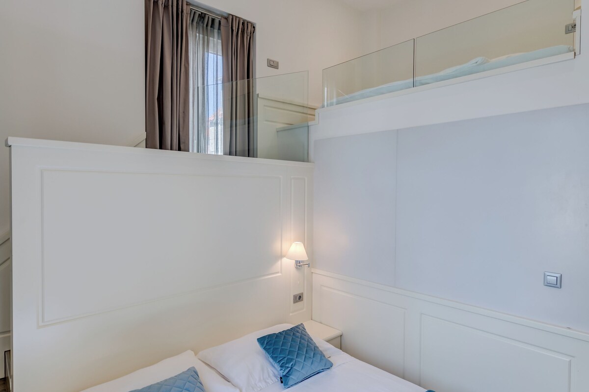 A bedroom with a bed, a window with curtains, a mirror, and a light fixture.