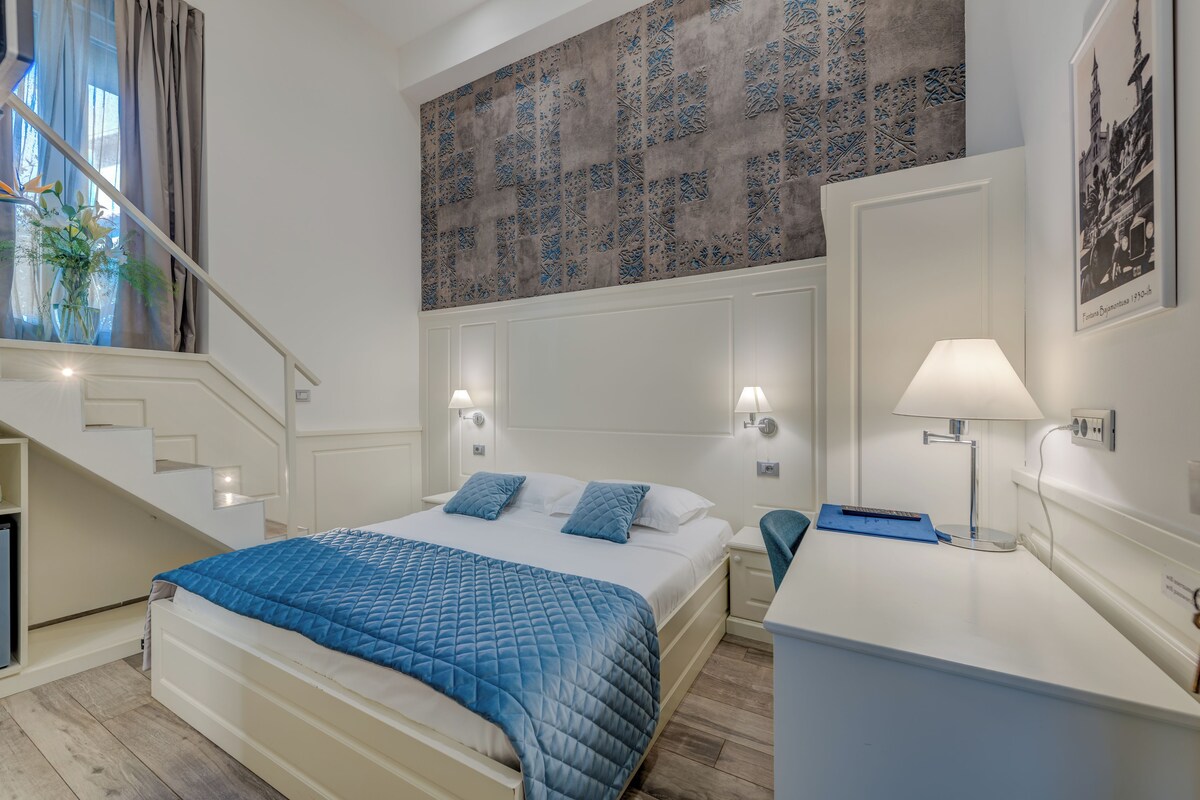 Un dormitorio con una cama, mesitas de noche, un escritorio, una lámpara y una escalera.