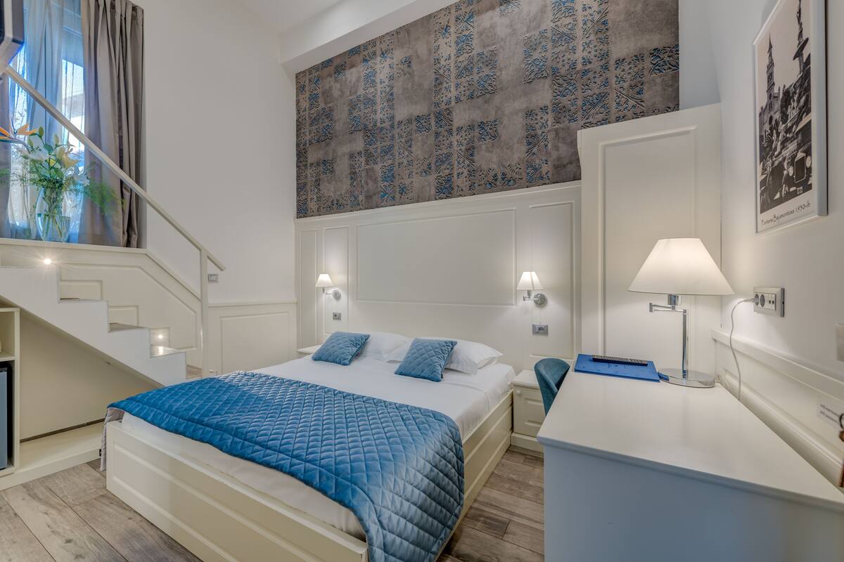 Un dormitorio con una cama, mesitas de noche, un escritorio, una lámpara y una escalera.