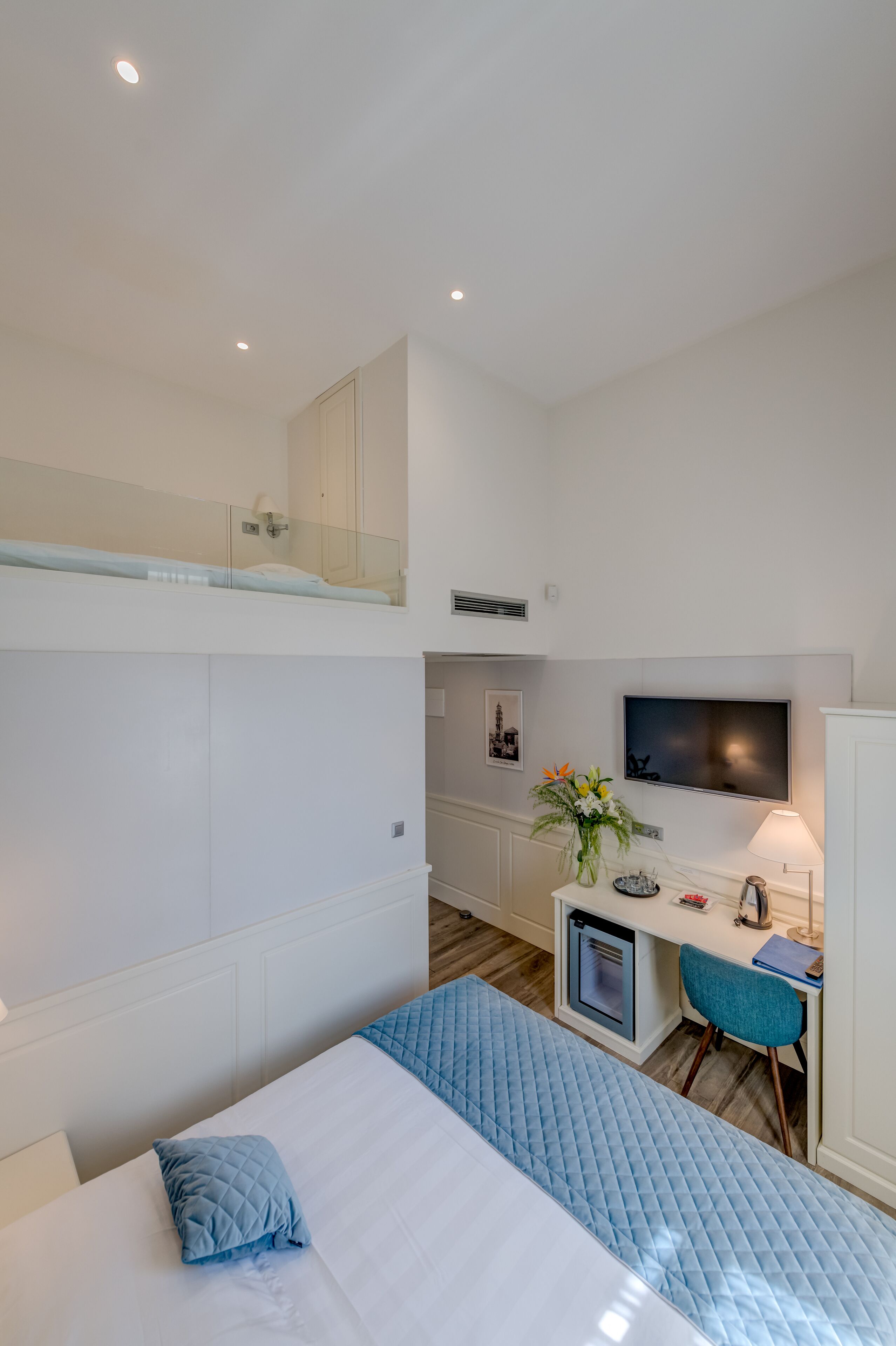 A hotel room with a bunk bed, a desk with a computer, a TV, and a small kitchenette.