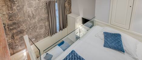 A bedroom with a bed, a glass railing, a wardrobe, and a patterned wall.