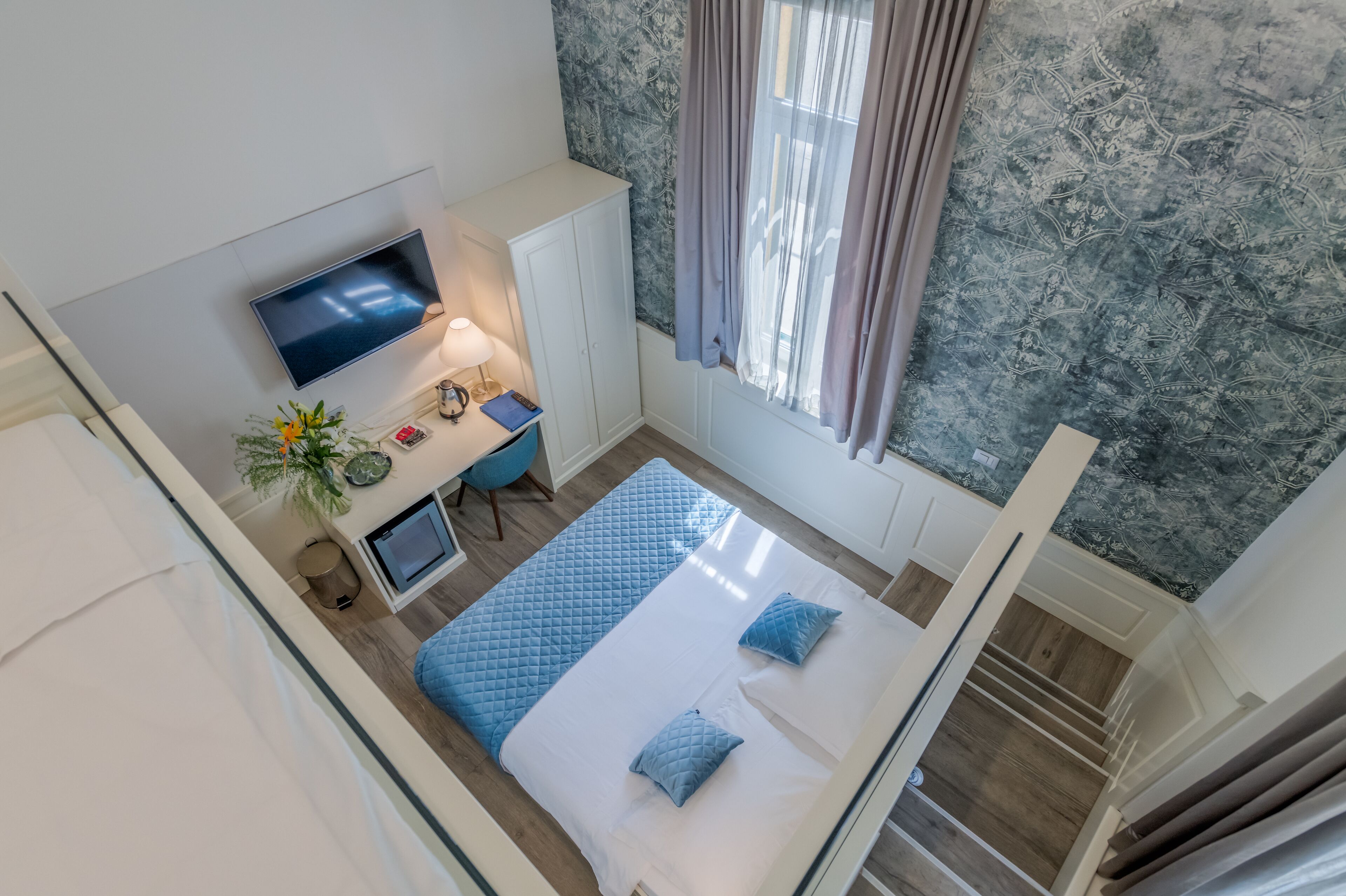 A bedroom with a bed, a desk, a TV, and a window with curtains.