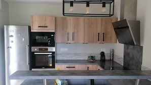 A modern kitchen with wooden cabinets, a stainless steel refrigerator, an oven, and a built-in island with a marble countertop. - Maison de Campagne (Larrivière-Saint-Savin)