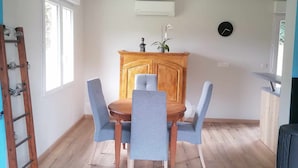 A dining area with a wooden table and blue chairs, a wooden cabinet, a clock on the wall, and a TV on the right. - Maison de Campagne (Larrivière-Saint-Savin)