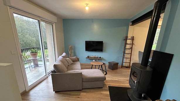 A living room with a sofa, a TV, a fireplace, and a balcony with outdoor furniture. - Maison de Campagne (Larrivière-Saint-Savin)