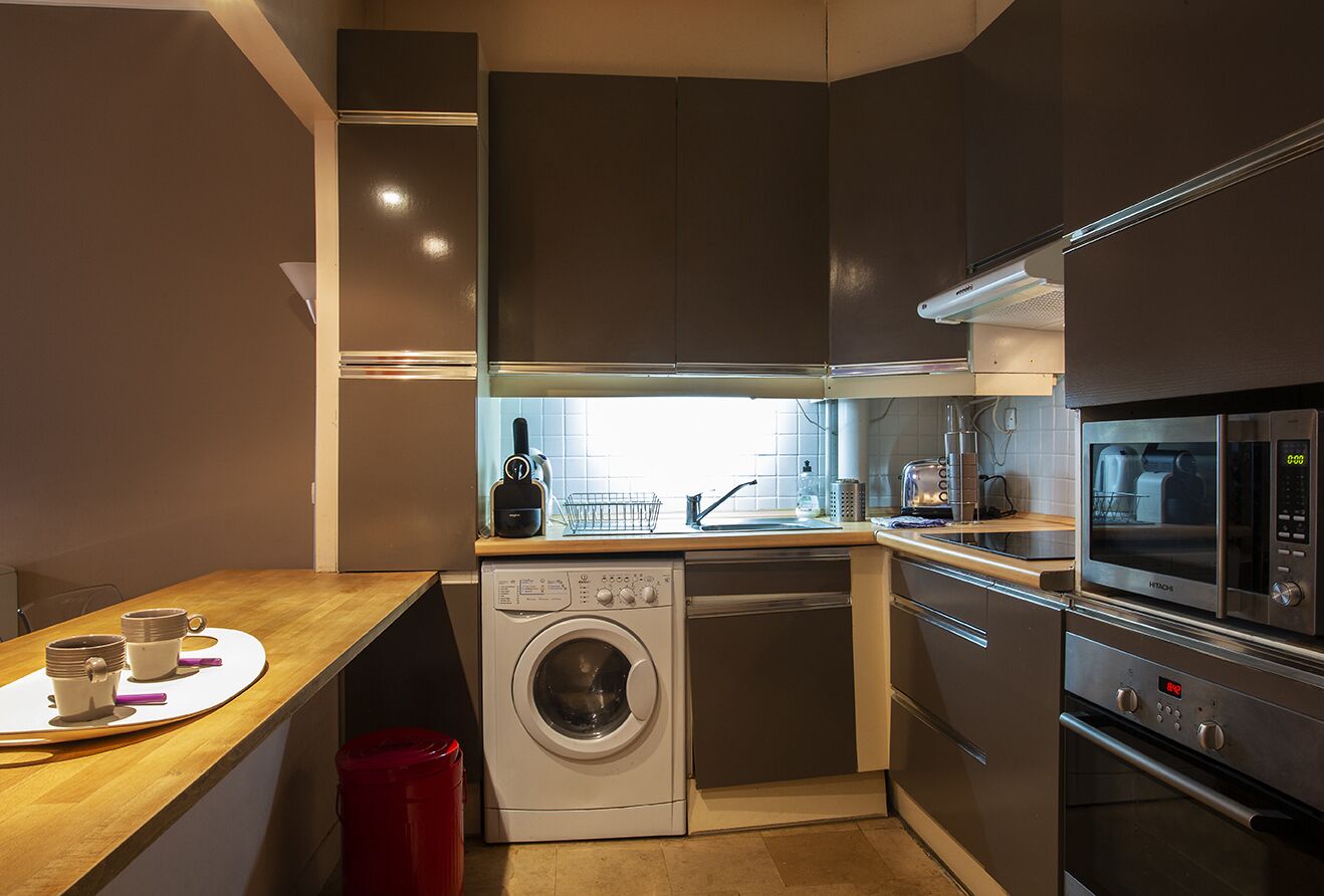 Une cuisine compacte équipée d’un lave-linge, d’un four à micro-ondes et d’un évier.