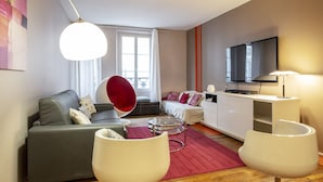 A modern living room with a grey sofa, a red egg chair, a round coffee table, and a flat-screen TV mounted on the wall. - Saint Honoré Opéra Louvre (Paris)