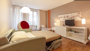 A modern hotel room with a bed, a red chair, a TV, and a desk.