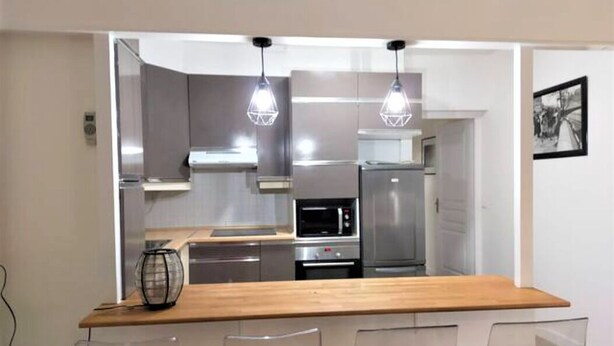 A modern kitchen with a wooden countertop, stainless steel appliances, and clear chairs. - Saint Honoré Opéra Louvre (Paris)