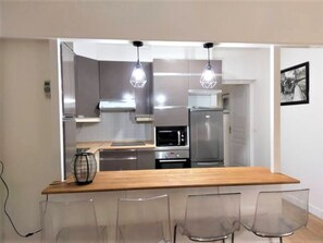 A modern kitchen with a wooden countertop, stainless steel appliances, and clear chairs.