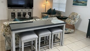 Un salon équipé d’un téléviseur à écran plat, d’une table à manger avec des tabourets de bar, d’un canapé et d’un fauteuil.