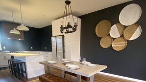 A modern kitchen with a central island, pendant lighting, and a dining area with a bench. - Modern Oasis (Prince George)