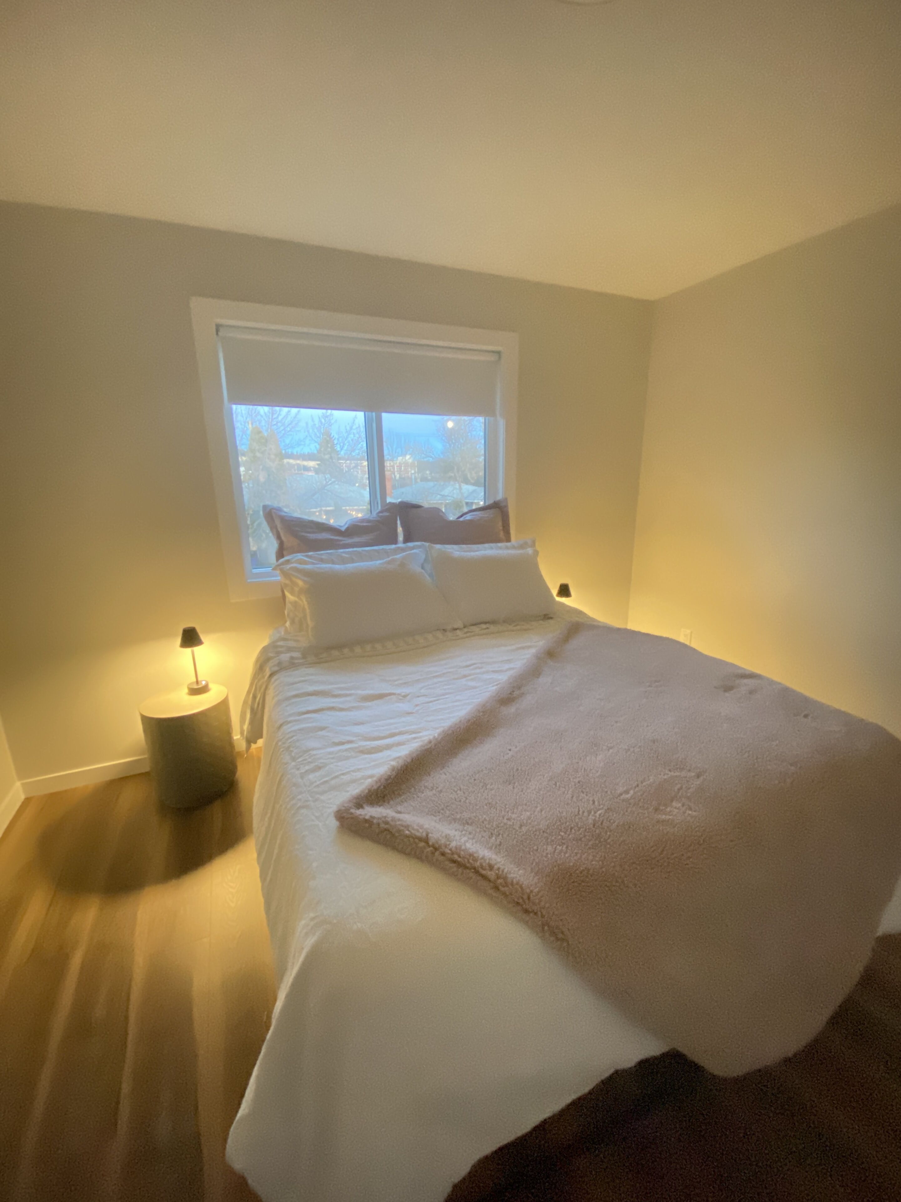 A bedroom with a bed, a window, a bedside lamp, and a nightstand.